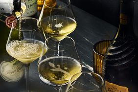 Bottles of Cava on a dark tabletop being poured into sparkling wine glasses