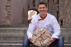 Michael Kress, a bread sommelier, sitting on the steps holding bread 