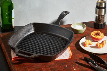 The Lodge Seasoned Cast Iron Square Grill Pan staged on a table next to a grilled peach.