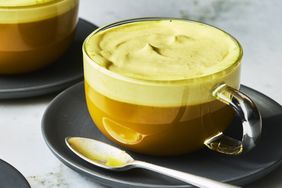 Haldi with a thick yellow foam in clear curved latte mug on white marble background