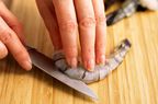 A person deveins a shrimp on a cutting board