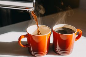 Hot coffee being poured into red mugs. 