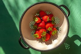 A colander full of strawberries on a green surface.