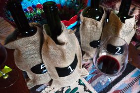 Four bottles in burlap bags numbered 1, 2, 3, and 5 with red wine in a glass