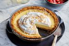 A Lemon Coconut Tart in a pie plate, next to a bowl of strawberries. 