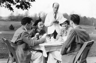 UNITED STATES - Circa 1930s: Waiter White Jacket Taking Order From Two Couples At Table Outdoors Alfresco Country Club.