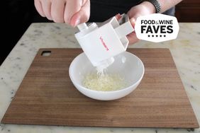 Person using Vivaant Cheese Grater to grate cheese into a bowl on a wooden cutting board