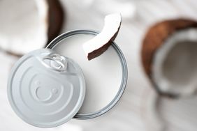 Canned coconut milk seen top down with coconuts in the background