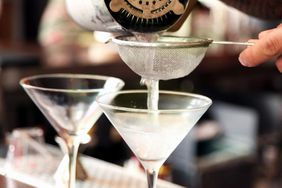 Pouring martini from cocktail shaker into frosted glass